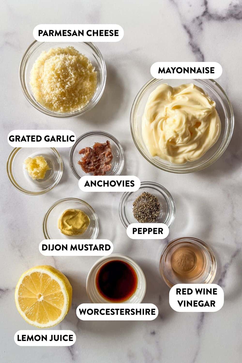 Caesar dressing ingredients in bowls on a marble background.