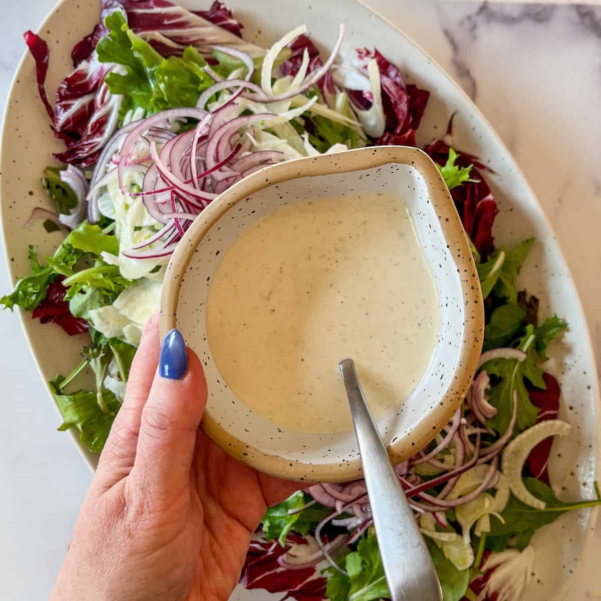 Caesar salad dressing being hold over a salad.