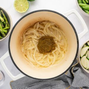 Cooking onions and green curry paste in a white dutch oven.