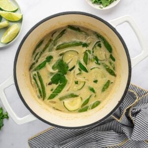 Vegetables with onions, green curry paste, and coconut milk in a white dutch oven.