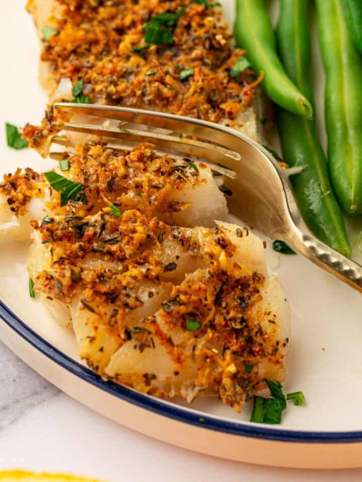 A gold fork cutting into a piece of baked cod.