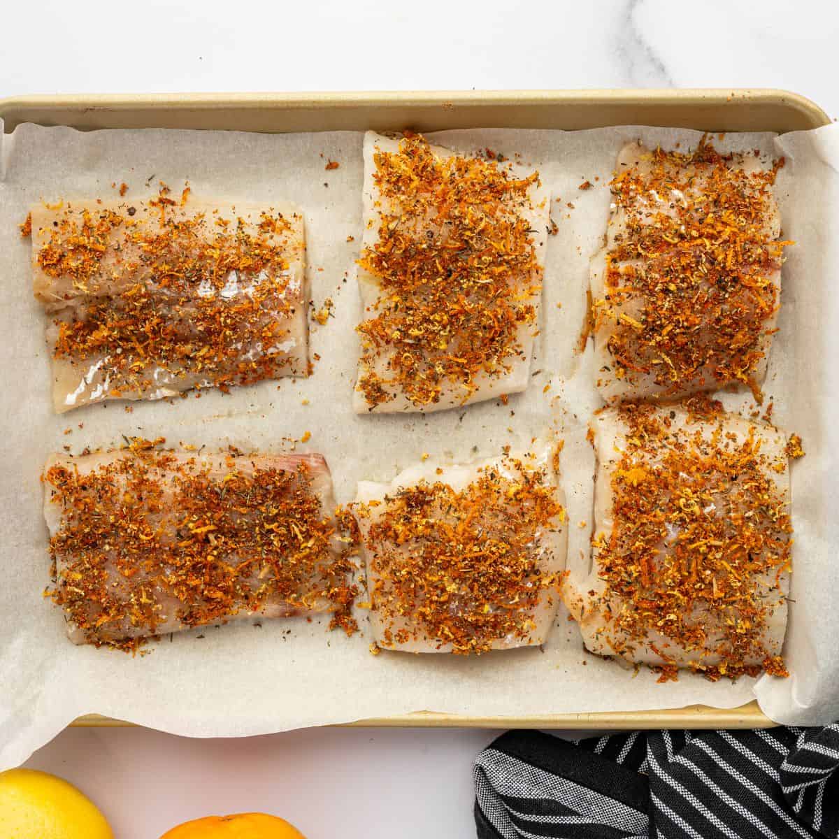Cod topped with spices on a parchment lined baking sheet.