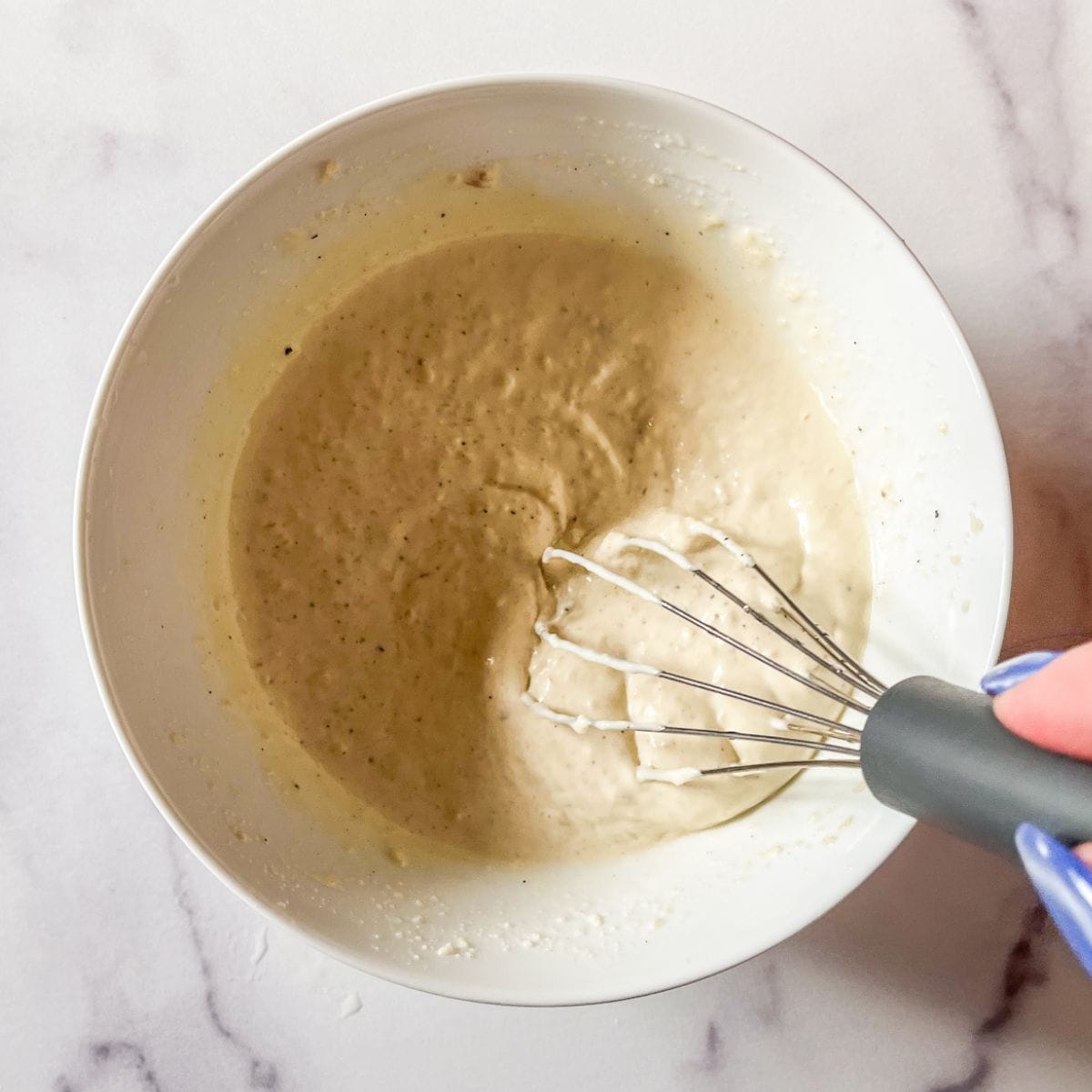 Homemade caesar dressing being whisked in a white bowl.