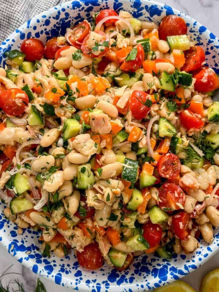 Tuna white bean salad with vegetables and herbs in a blue and white speckled bowl with a silver spoon.