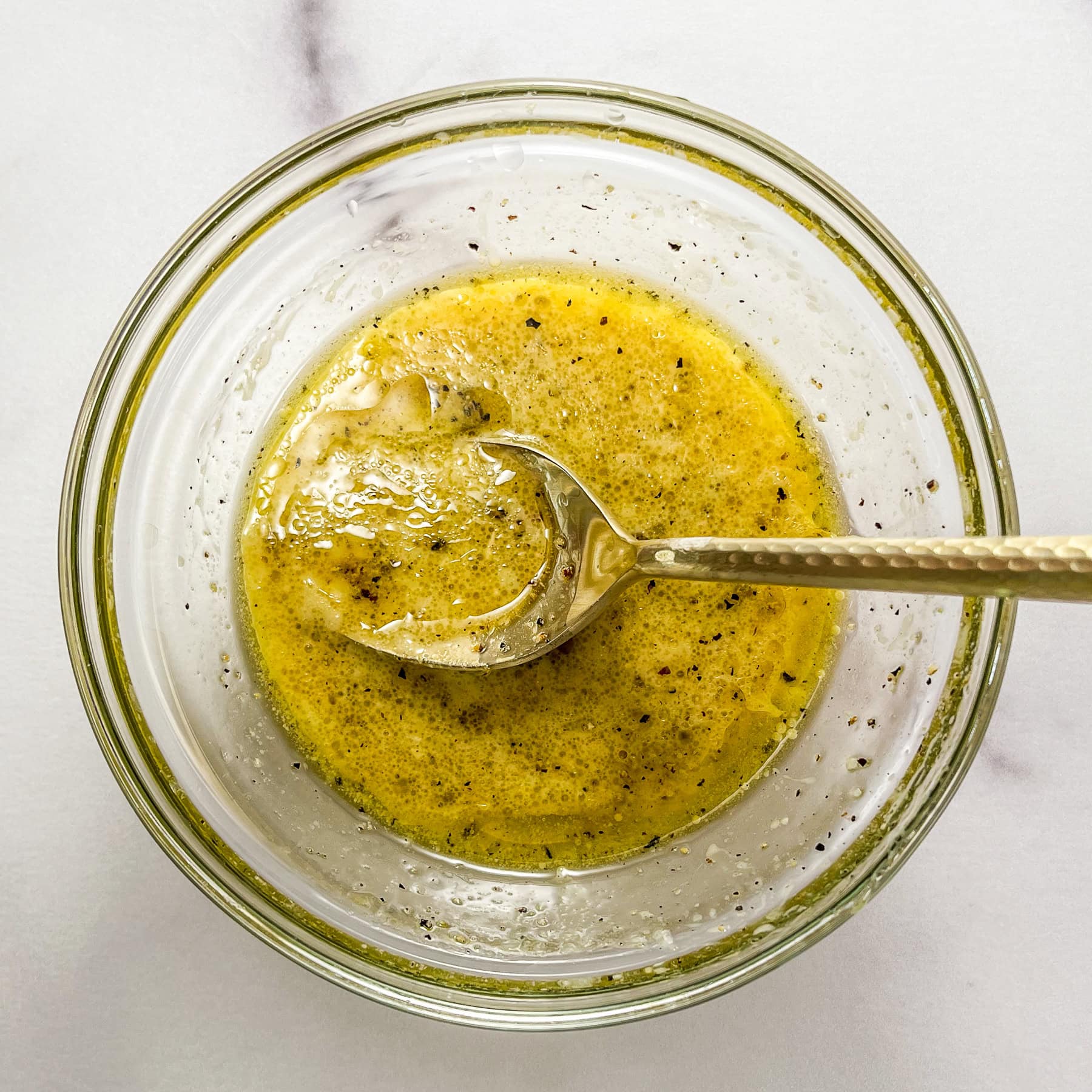 Salad dressing for white bean salad in a small glass bowl with gold spoon.