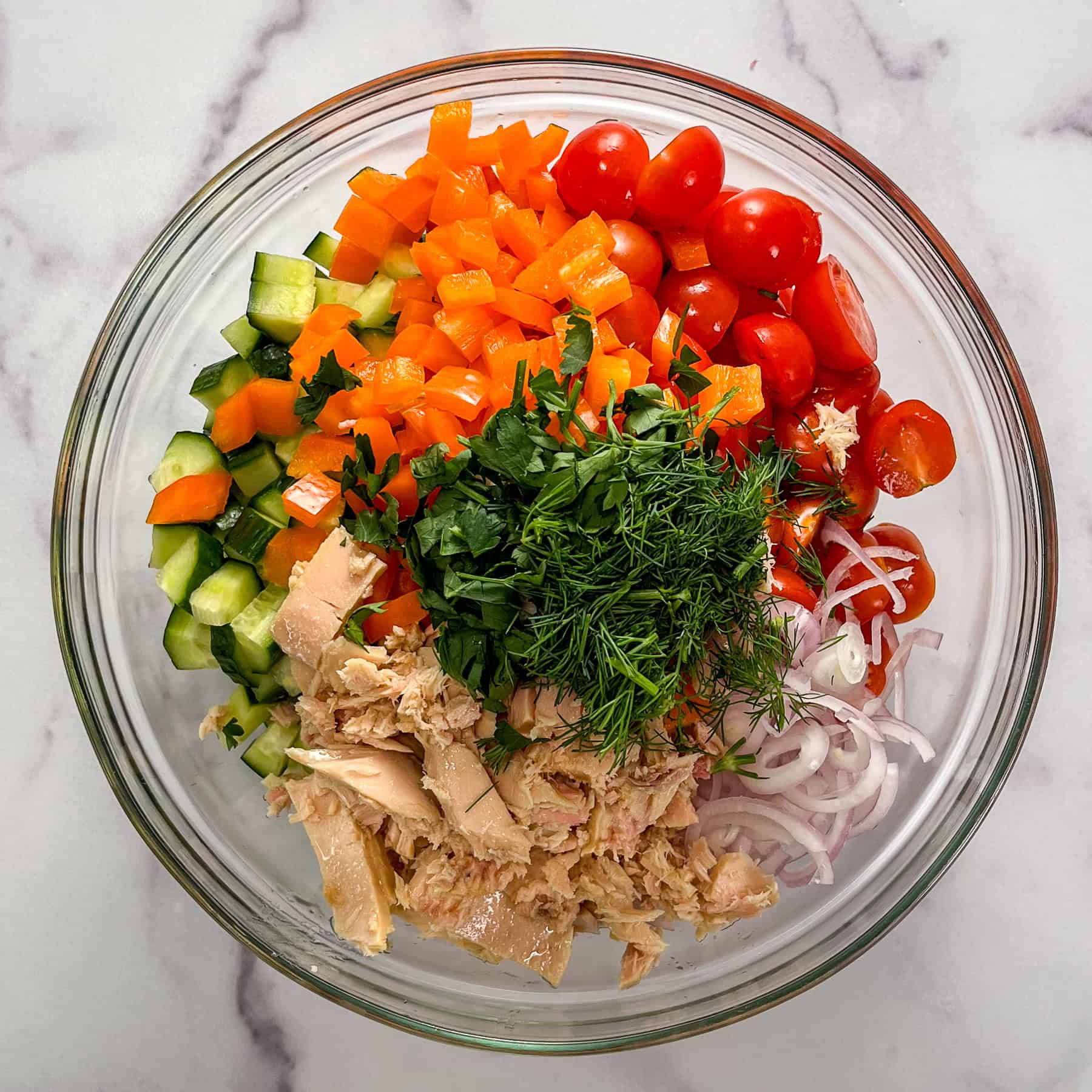 Chopped vegetables, herbs, and tuna in a glass bowl.
