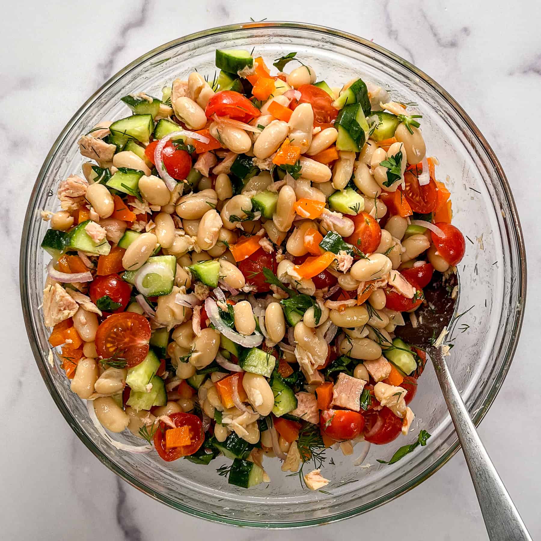 Tuna white bean salad with vegetables and herbs in a glass bowl.