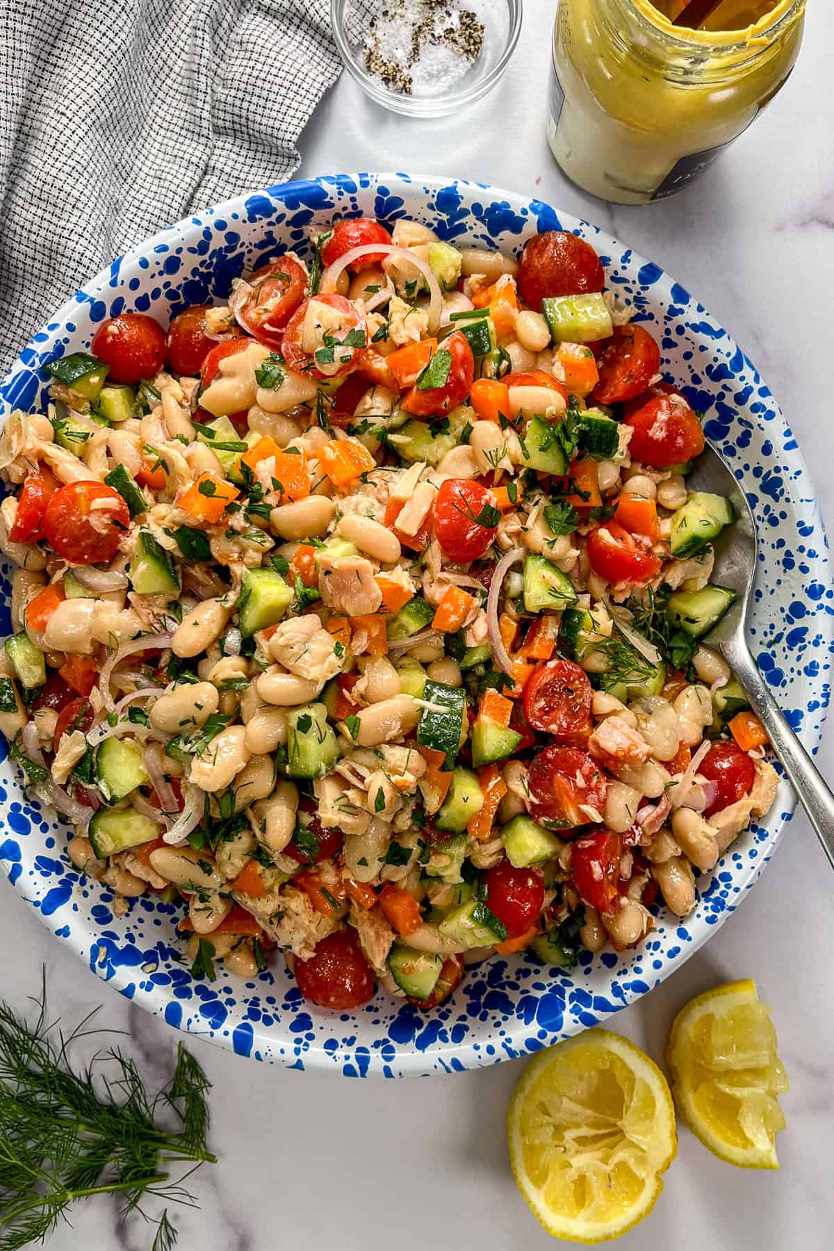 Tuna white bean salad with vegetables and herbs in a blue and white speckled bowl with a silver spoon.