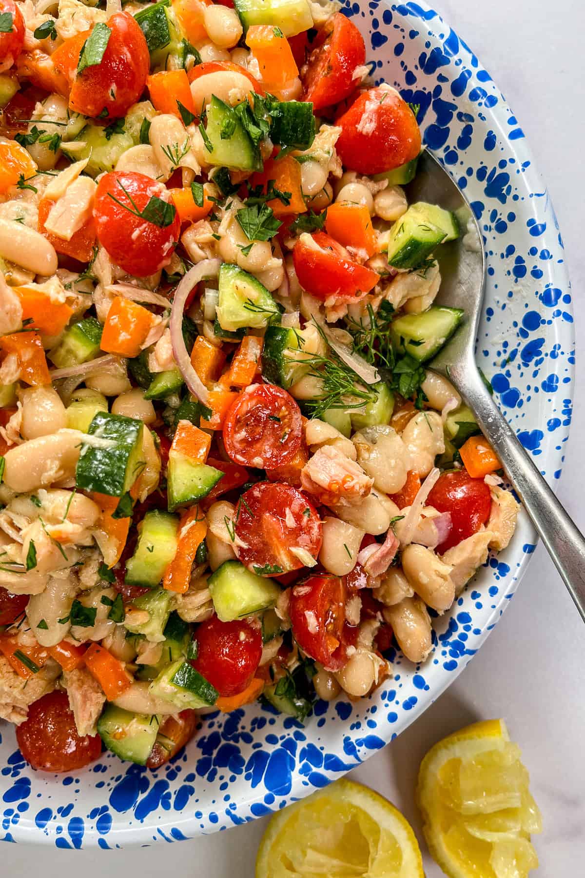 Tuna white bean salad with vegetables and herbs in a blue and white speckled bowl with a silver spoon.