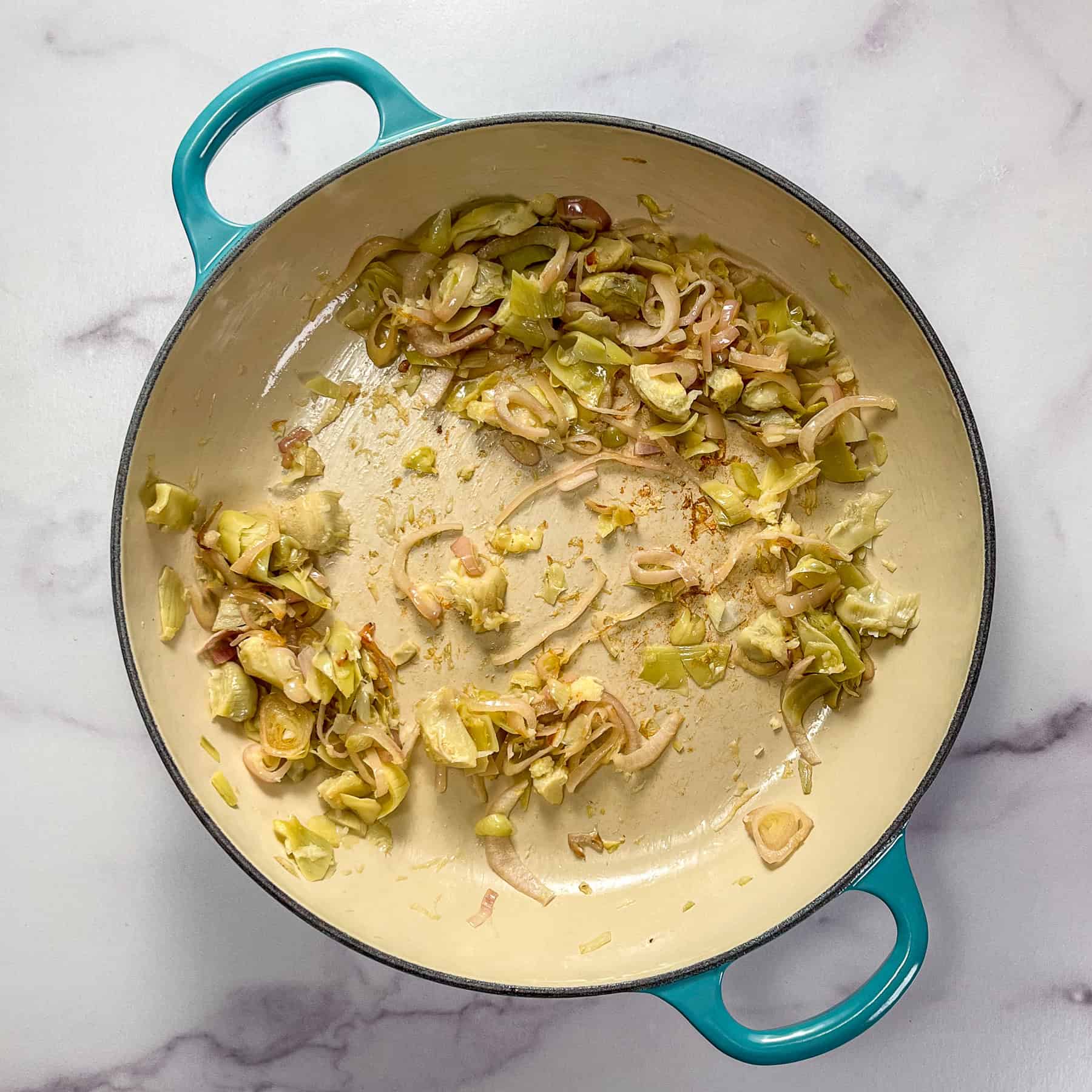 Shallots, chopped artichoke hearts, and garlic cooking in a braiser pan.