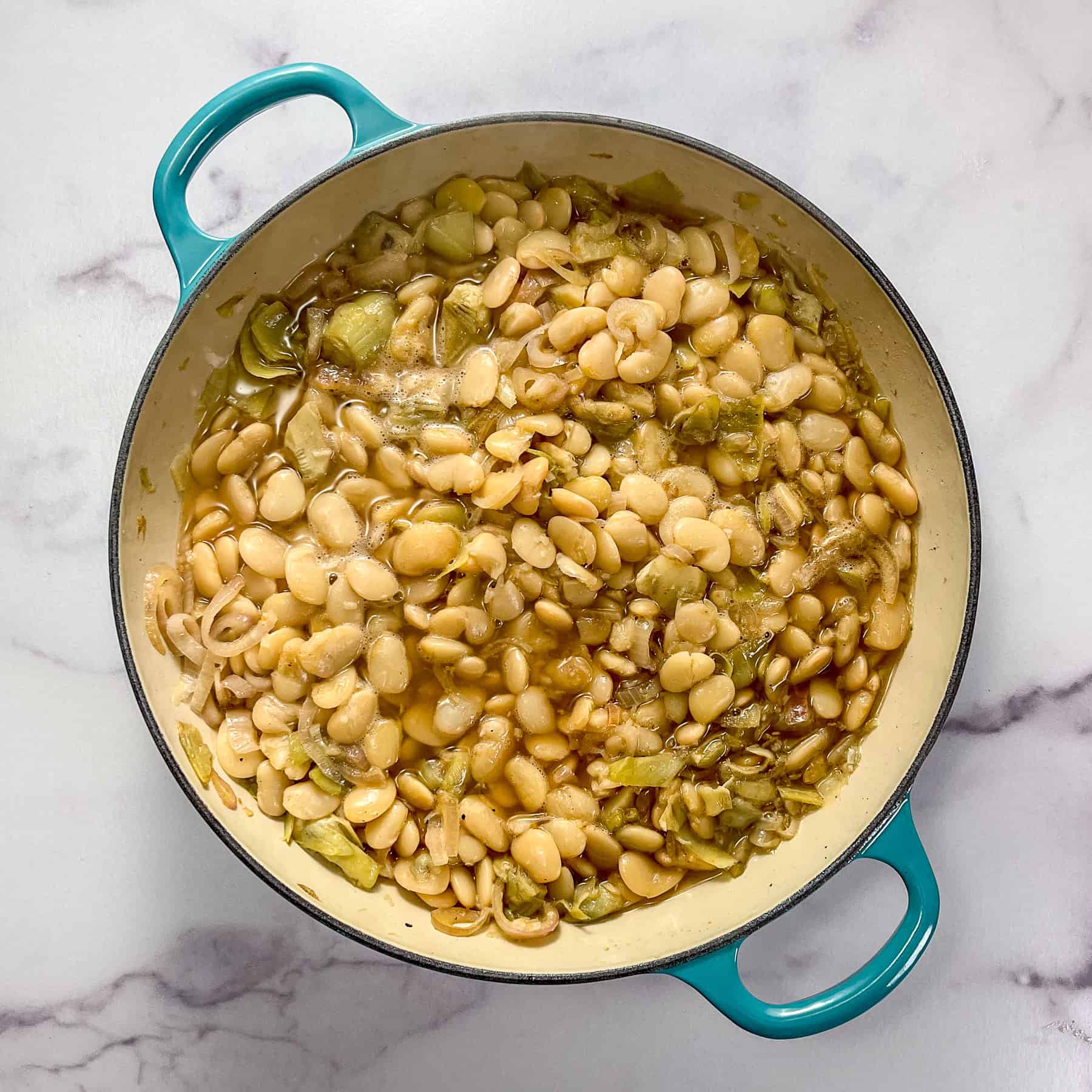 Butter beans, stock, and aromatics cooking in a braiser pan.