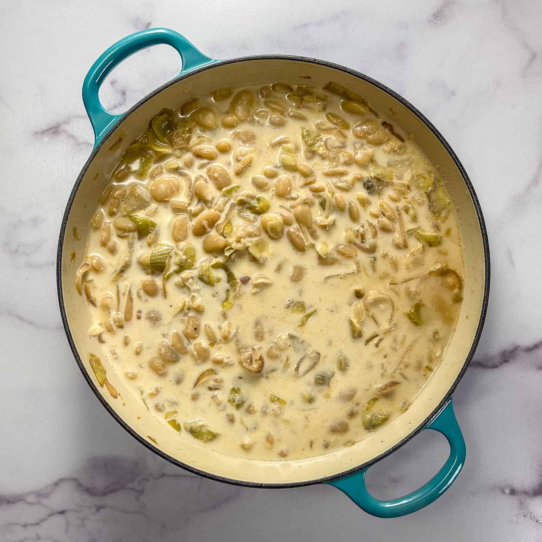 Butter beans, stock, heavy cream, and aromatics cooking in a braiser pan.