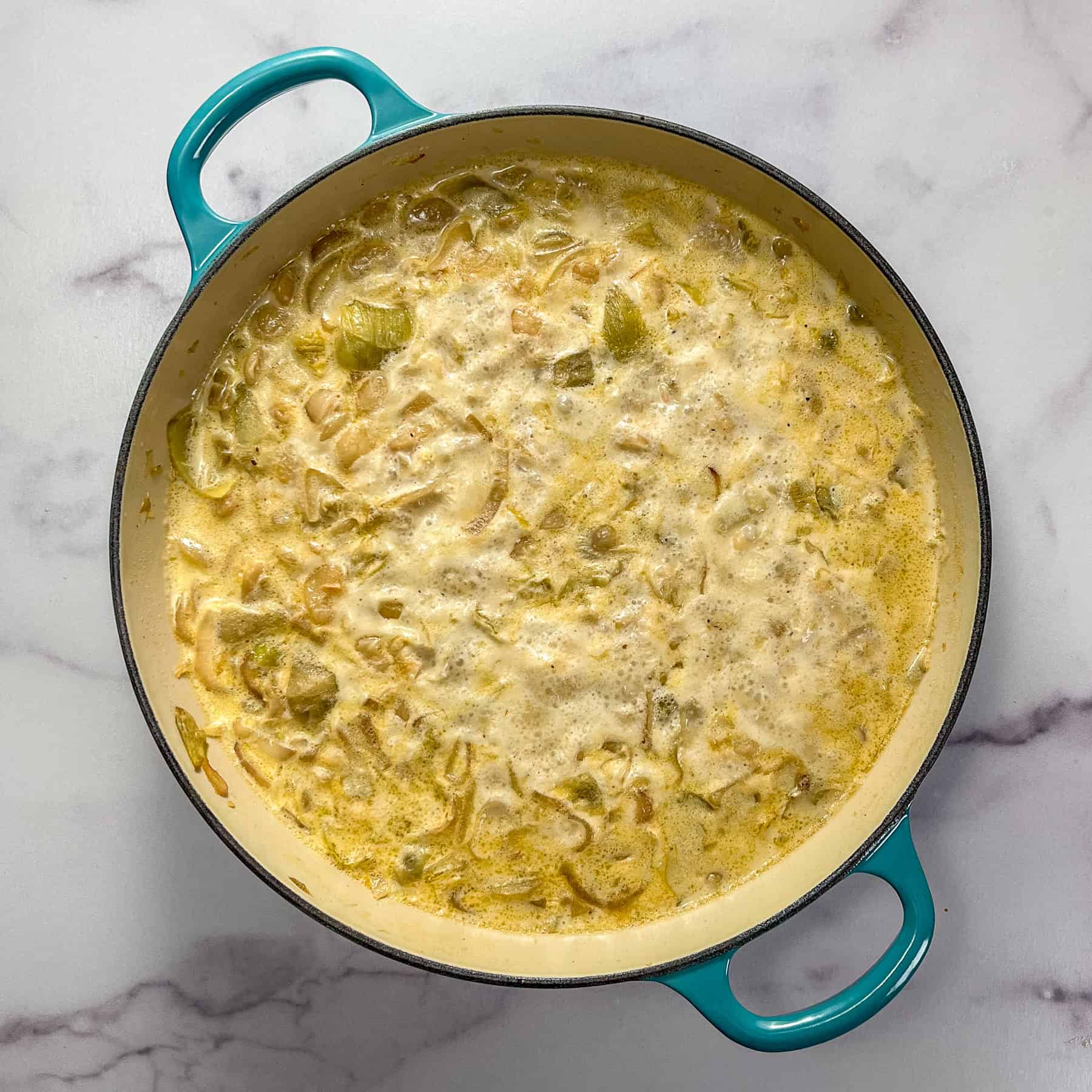 Butter beans, stock, heavy cream, and aromatics simmering in a braiser pan.