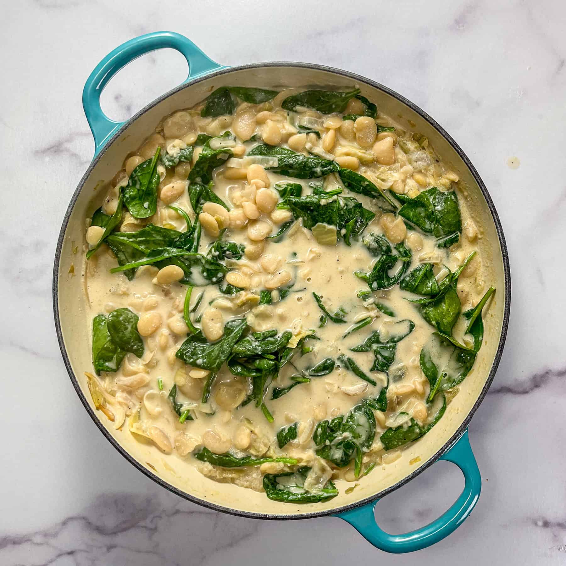 Spinach stirred into butter beans with cream, stock, aromatics, and artichokes.