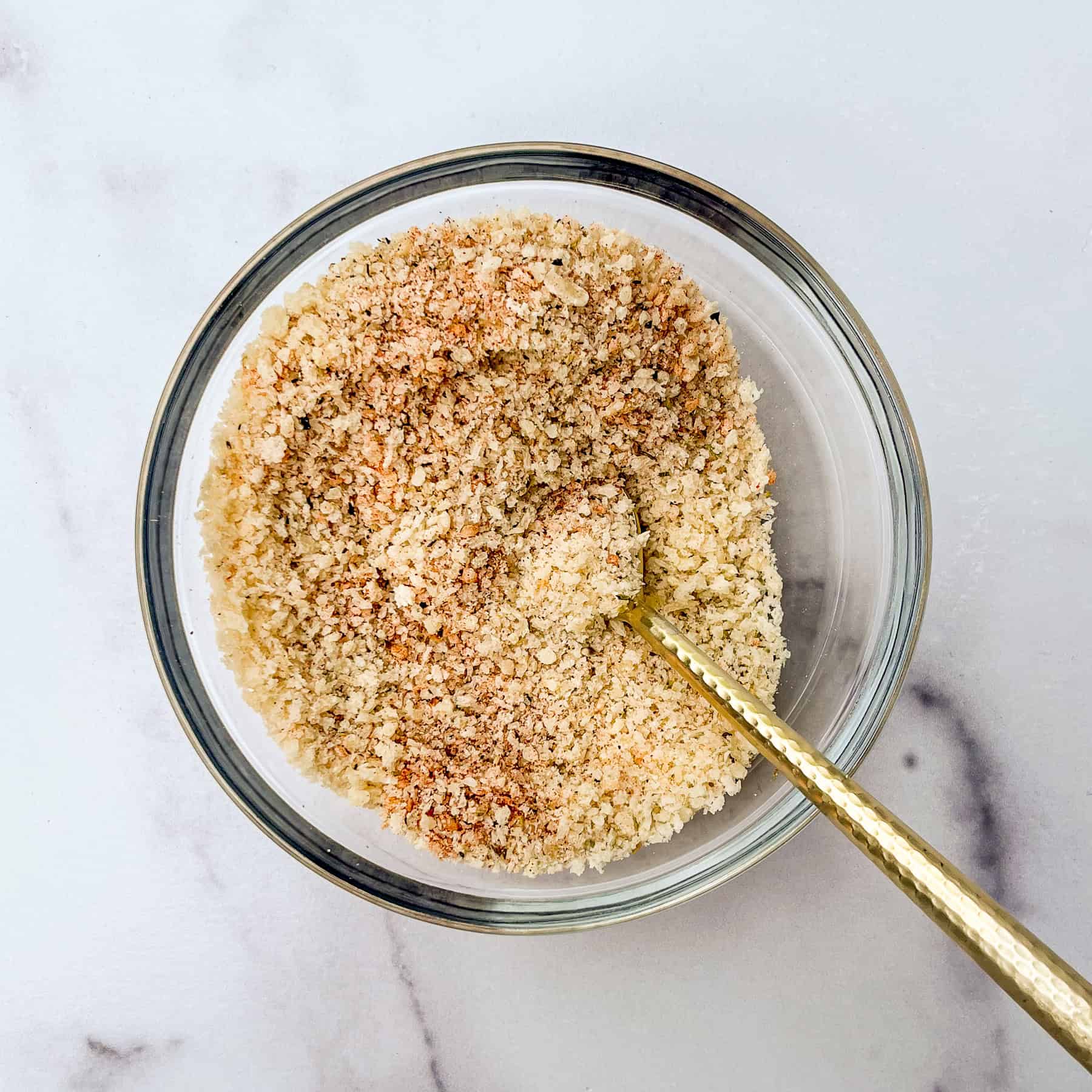 Panko, parmesan, and spices mixed in a glass bowl with gold spoon.