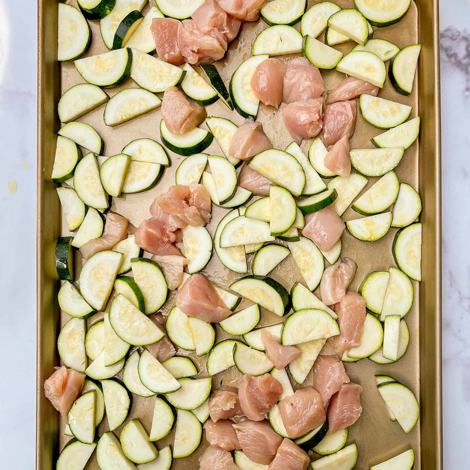 Sliced zucchini and chicken on a sheet pan.