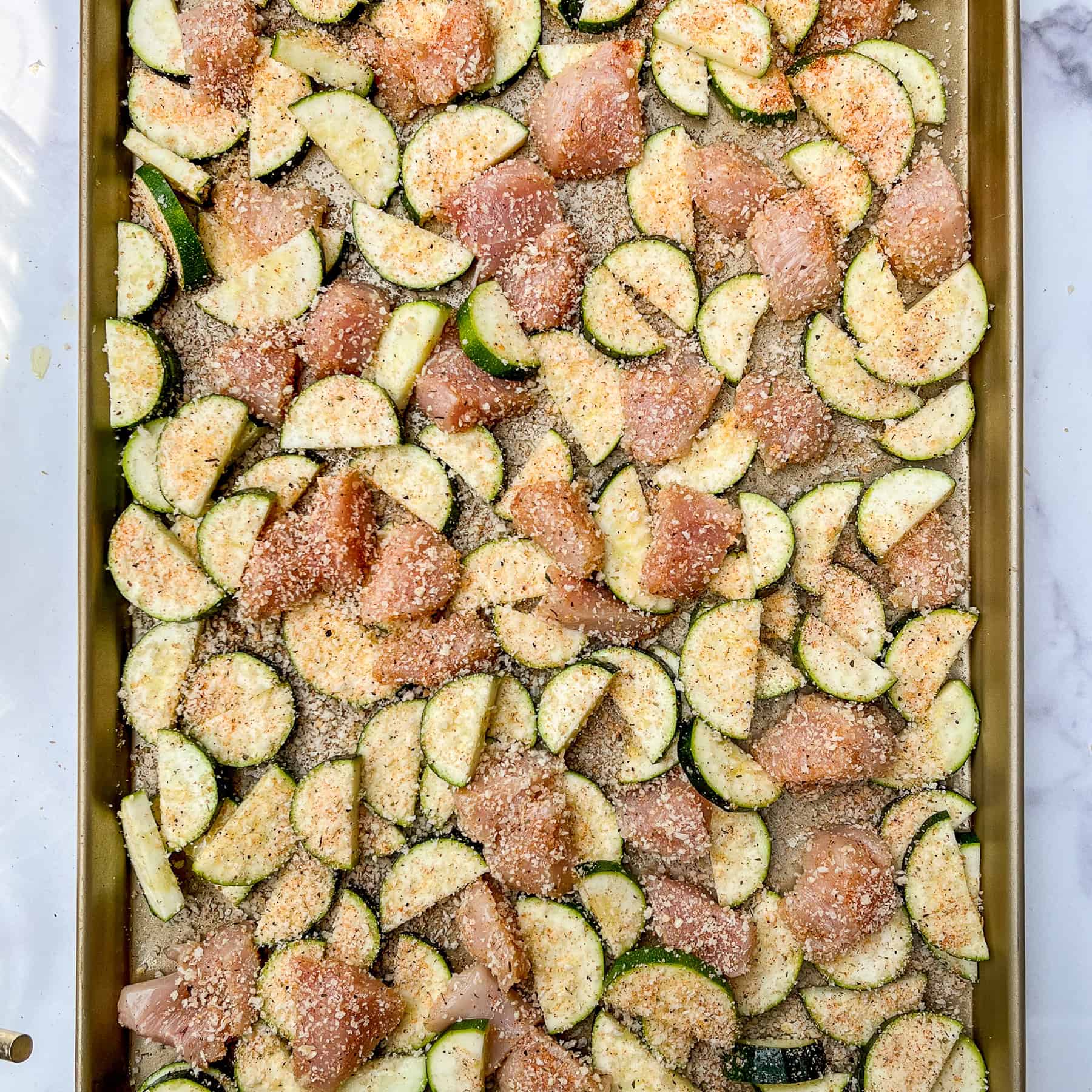 Sliced chicken and zucchini on a sheet pan topped with panko parmesan mixture.