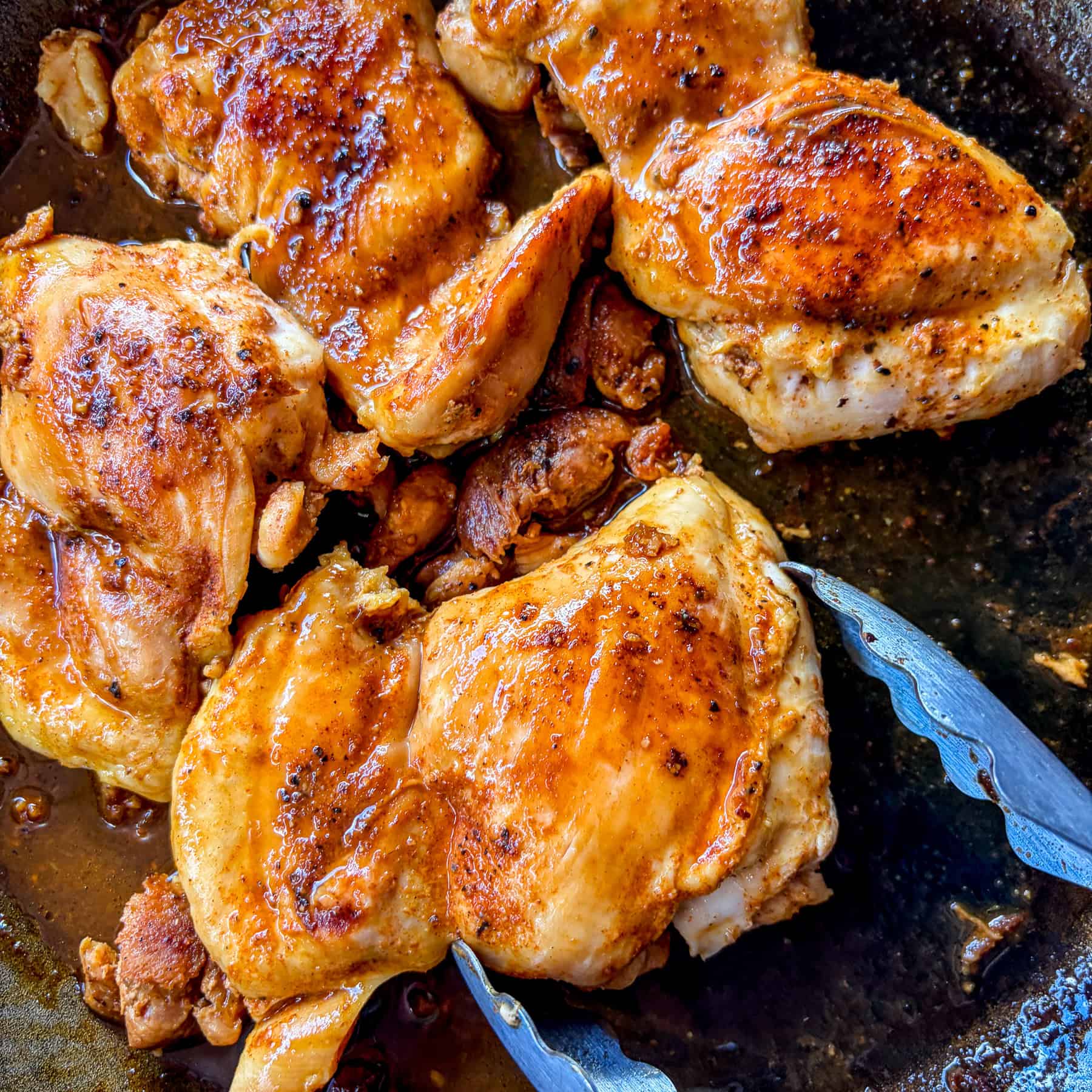 Easy sauteed chicken thighs in a skillet with tongs.