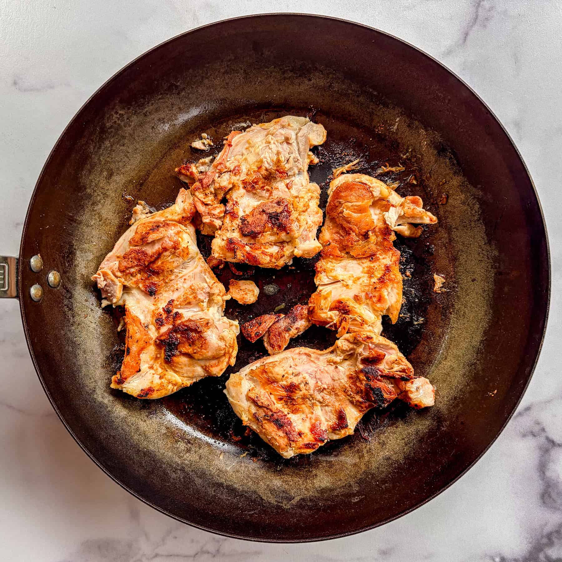 Chicken thighs cooking in a skillet.