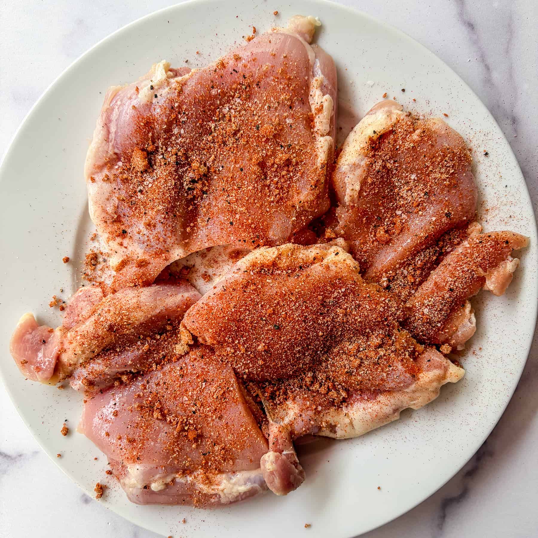 Raw chicken thighs seasoned with spices.