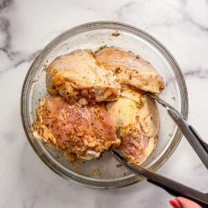 Chicken marinating in sauce in a glass bowl.