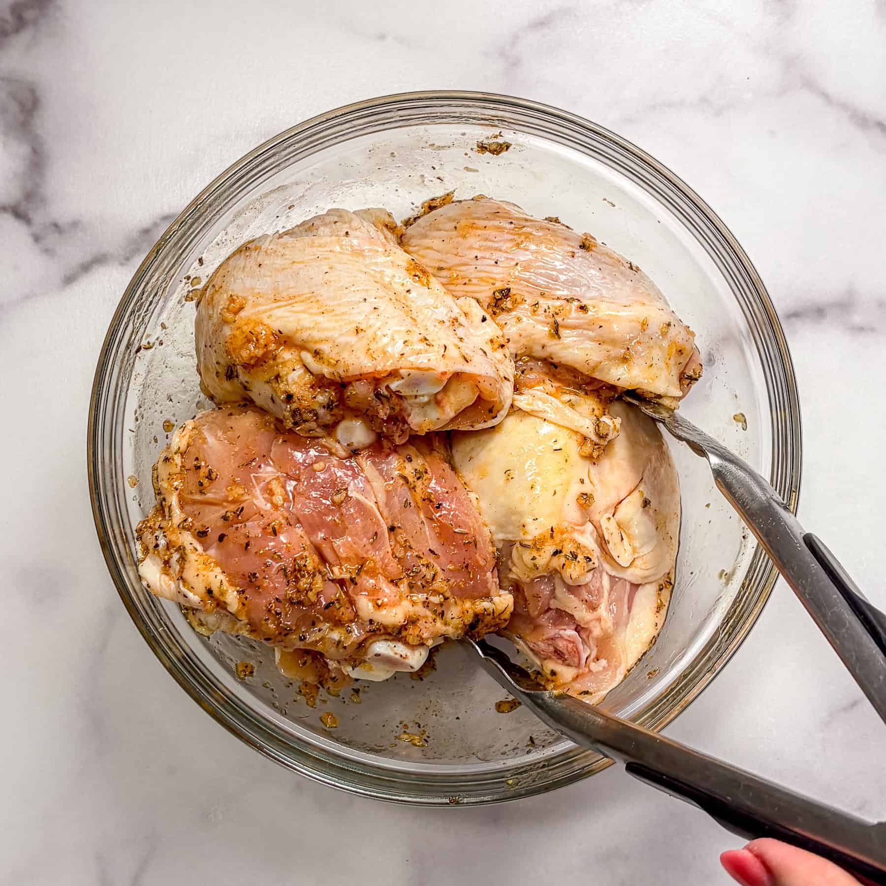 Chicken marinating in sauce in a glass bowl.