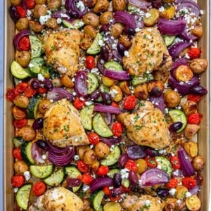 Greek chicken thighs, vegetables, and feta on a sheep pan.
