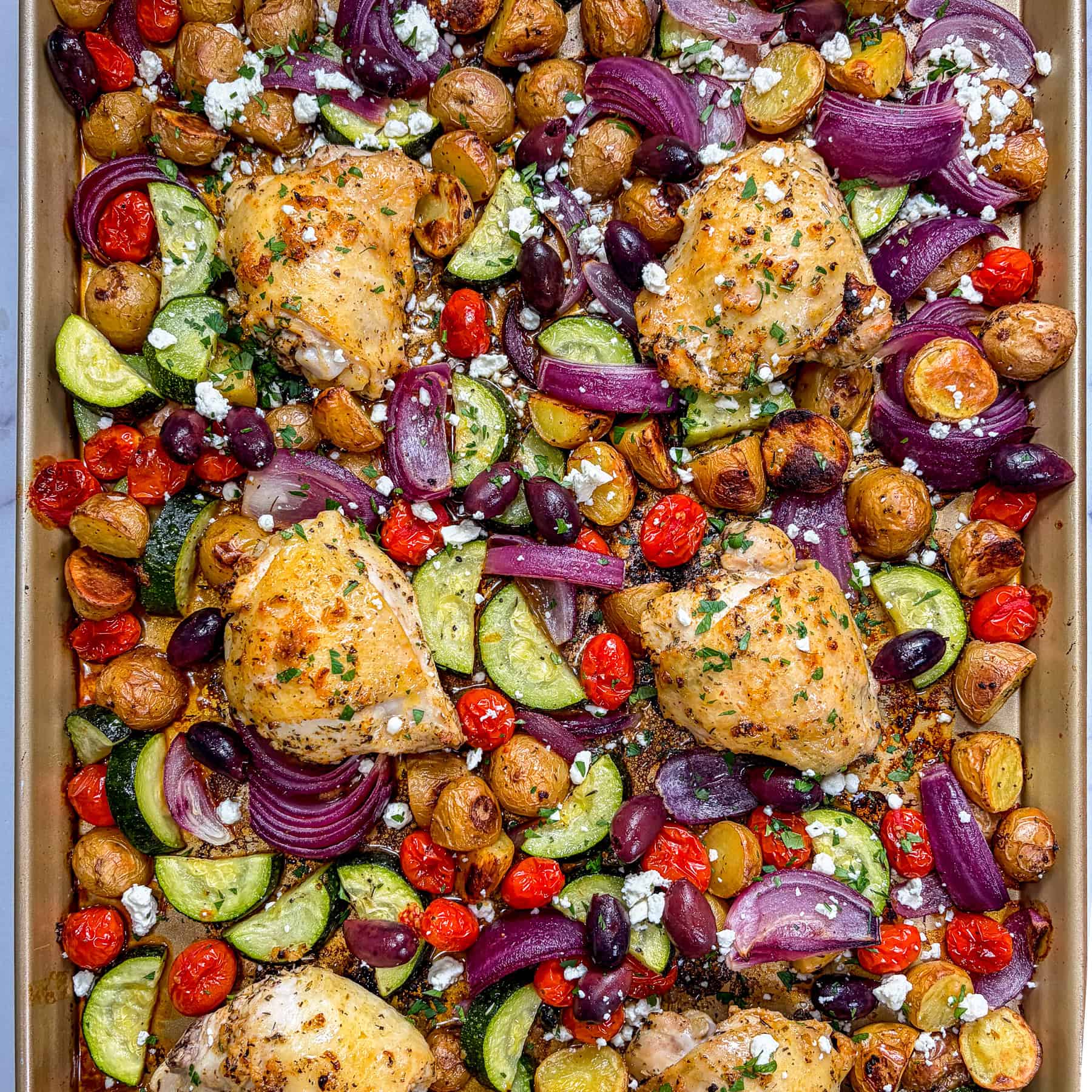 Greek chicken thighs, vegetables, and feta on a sheep pan.