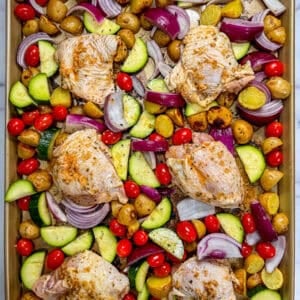 Raw chicken thighs and vegetables on a sheet pan.