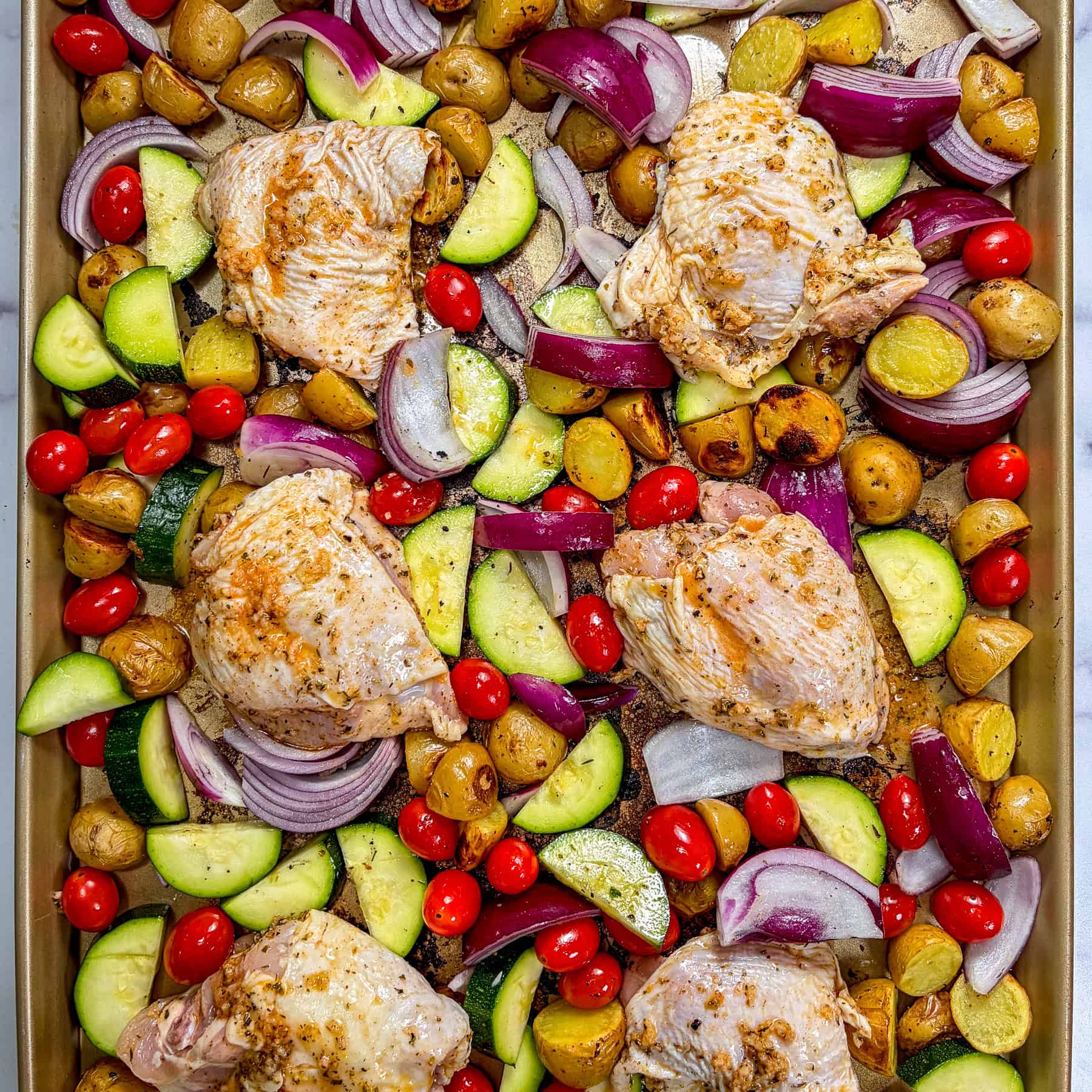 Raw chicken thighs and vegetables on a sheet pan.
