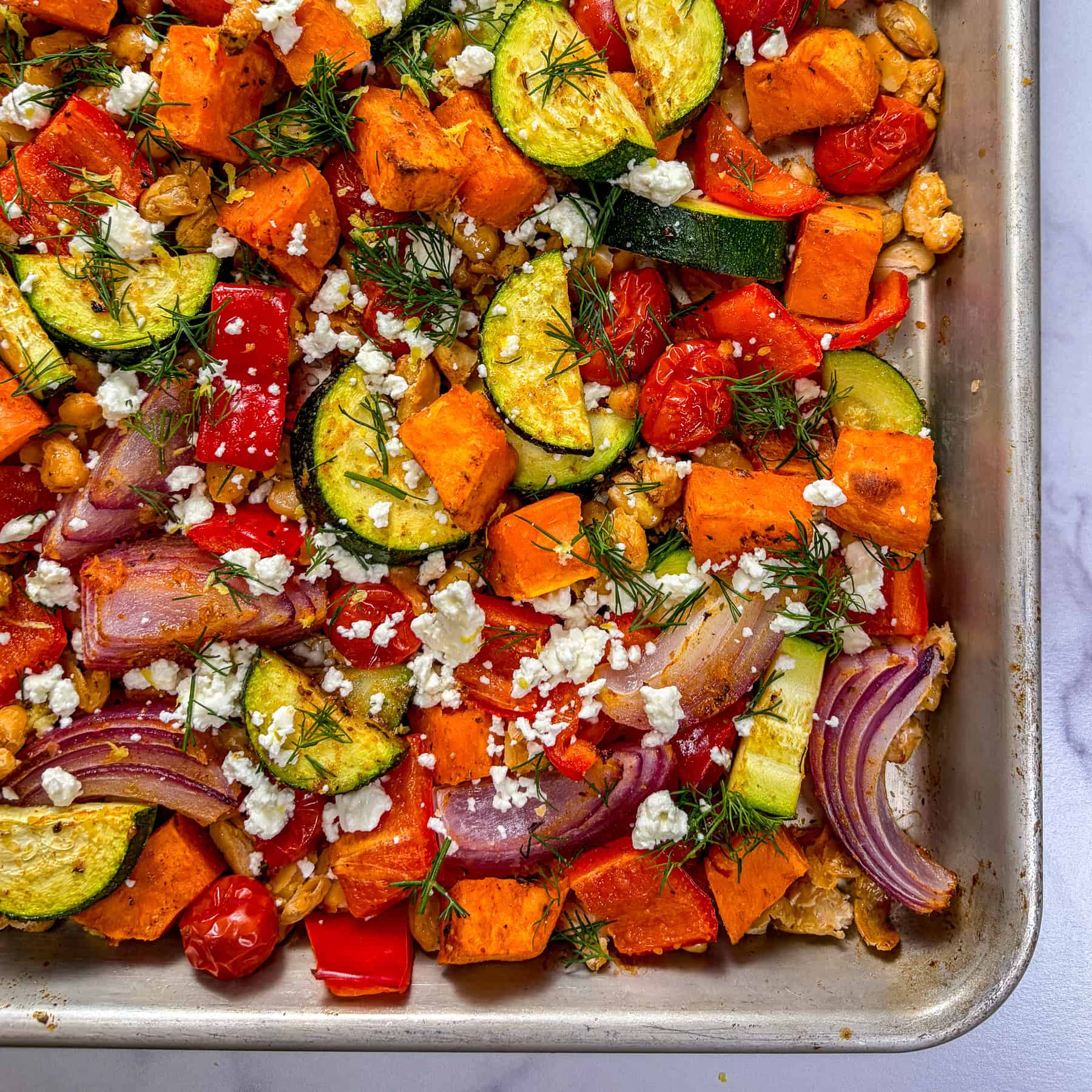 Roasted vegetables and white beans on a silver sheet pan.
