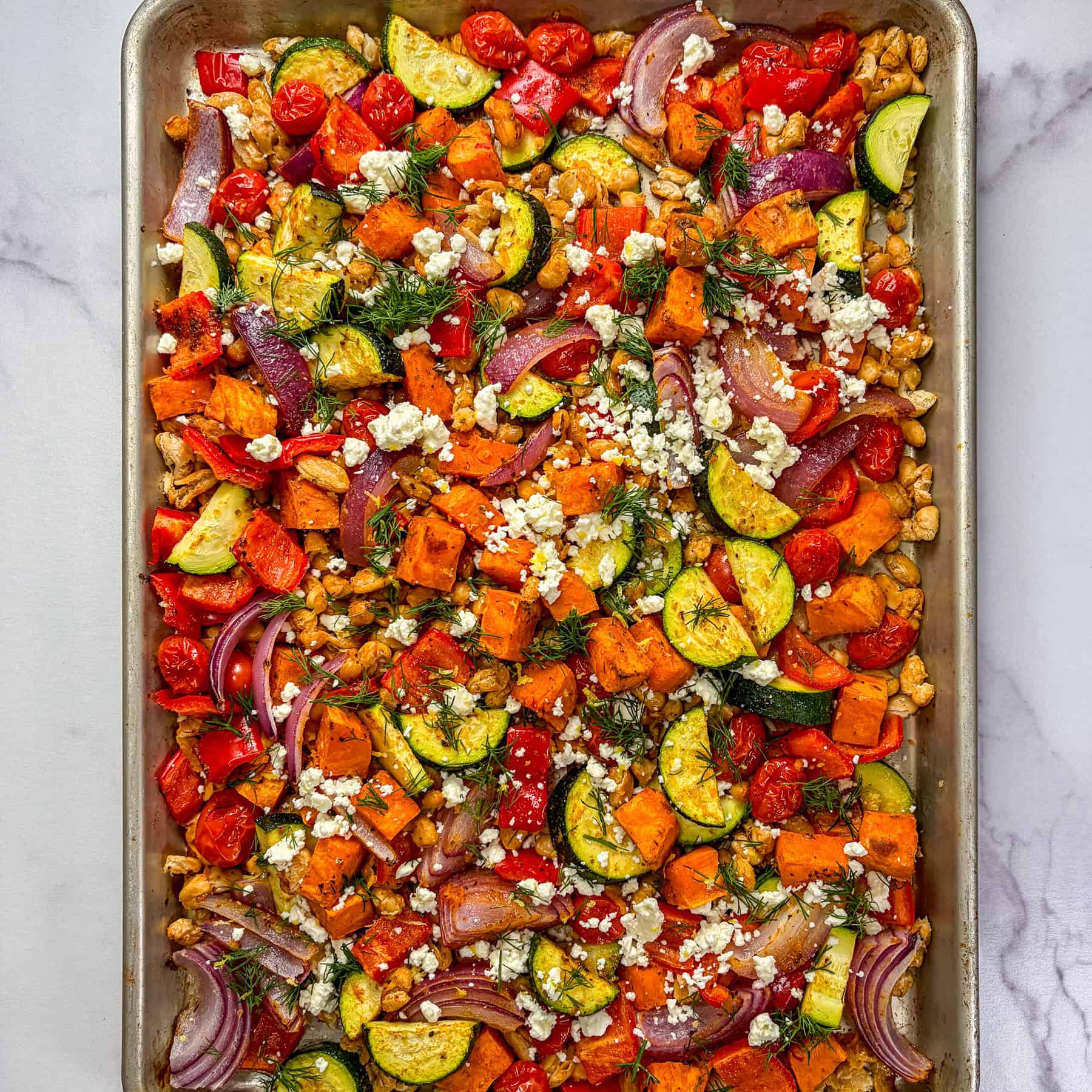 Roasted vegetables and white beans topped with feta and herbs on a sheet pan.