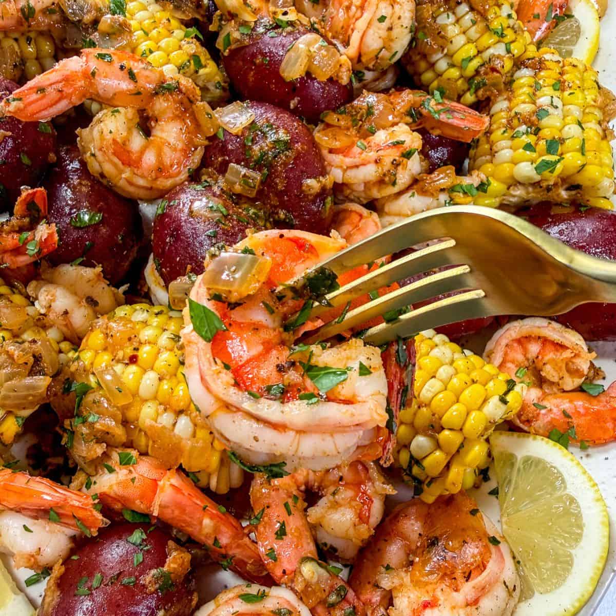 A gold fork picking up a shrimp from a seafood boil platter.