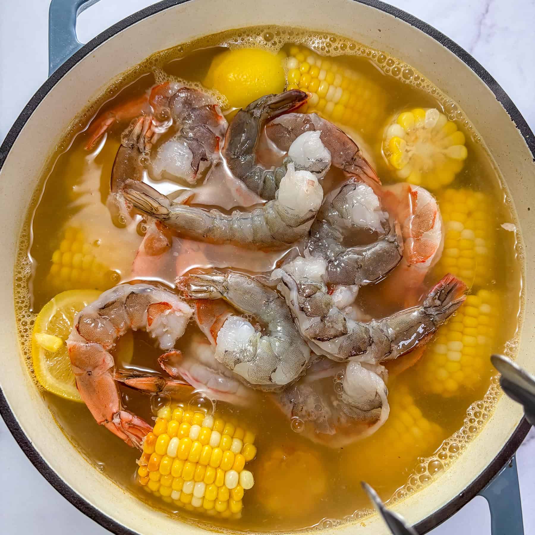 Shrimp being added to corn and potatoes in a large pot of water.