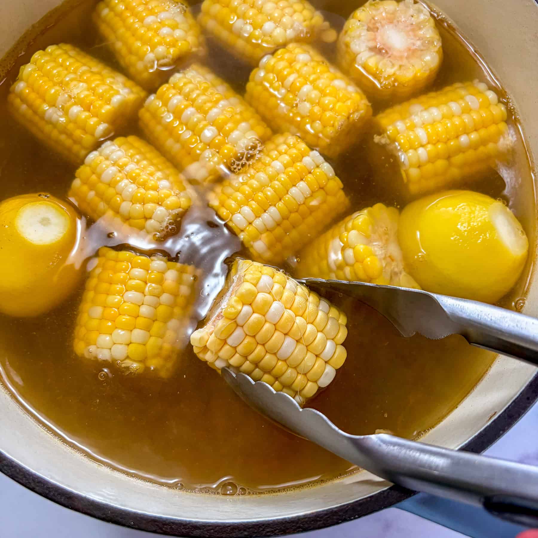 Corn and potatoes boiling in a large pot of water.
